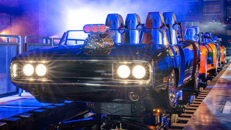 A front three-quarters shot of Dom's black Charger with its headlights on in front of the two orange cars on the ride