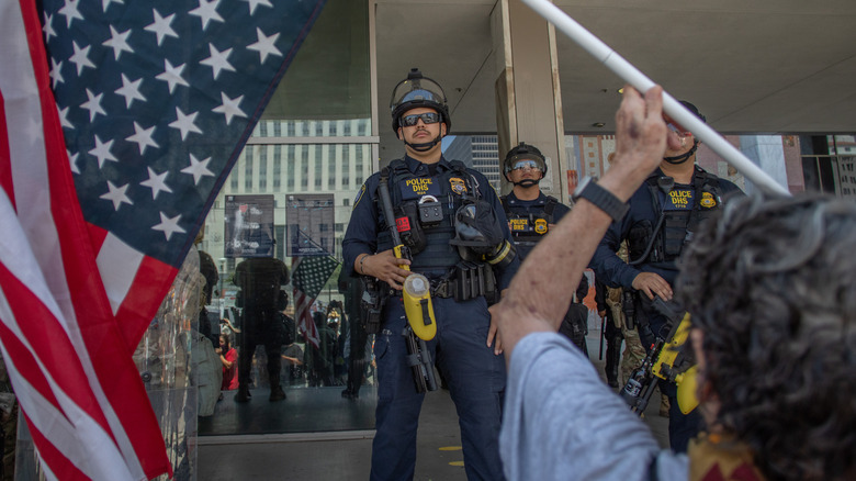 A Los Angeles protestor holds up an upside-down American flag in front of Department of Homeland Security "police" in January 2026.