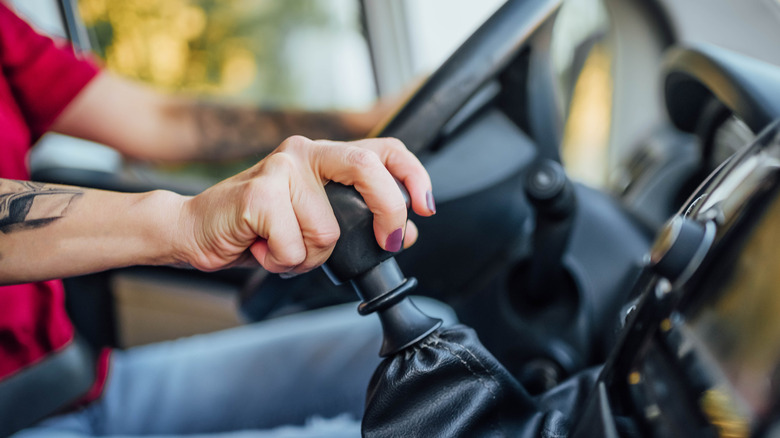 A close-up of a person resting a hand on a manual transmission lever in a car.