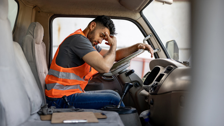 A fatigued driver rubs his forehead after a long day behind the wheel of his semi.